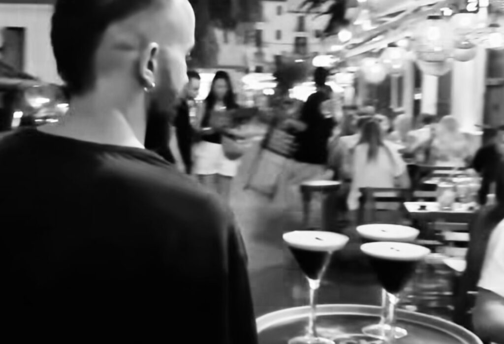 Camarero de La Bodega transportando varios Espresso Martinis entre las mesas de la terraza en una noche animada en Dalt Vila.
