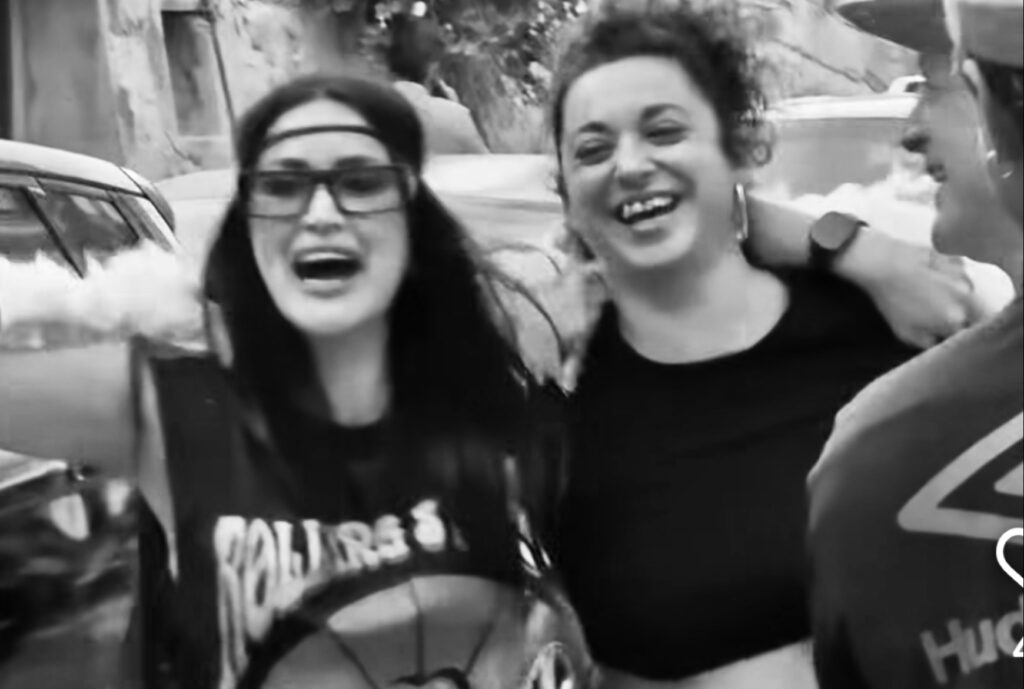 Dos amigas abrazándose y sonriendo frente a la entrada de La Bodega, compartiendo un momento espontáneo de alegría y amistad.